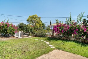 A garden with a paved path, flowering plants, and a stone wall. - Holiday Home 'Evans Terrace Suite' (Nikiana)