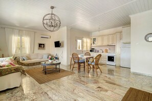 A spacious living room with a marble floor, a dining area with wicker chairs, and a kitchen with white cabinets and appliances. - Holiday Home 'Evans Terrace Suite' (Nikiana)