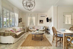 A well-lit living room with a chandelier, a sofa set, a coffee table, and a dining area with a chair and table. - Holiday Home 'Evans Terrace Suite' (Nikiana)