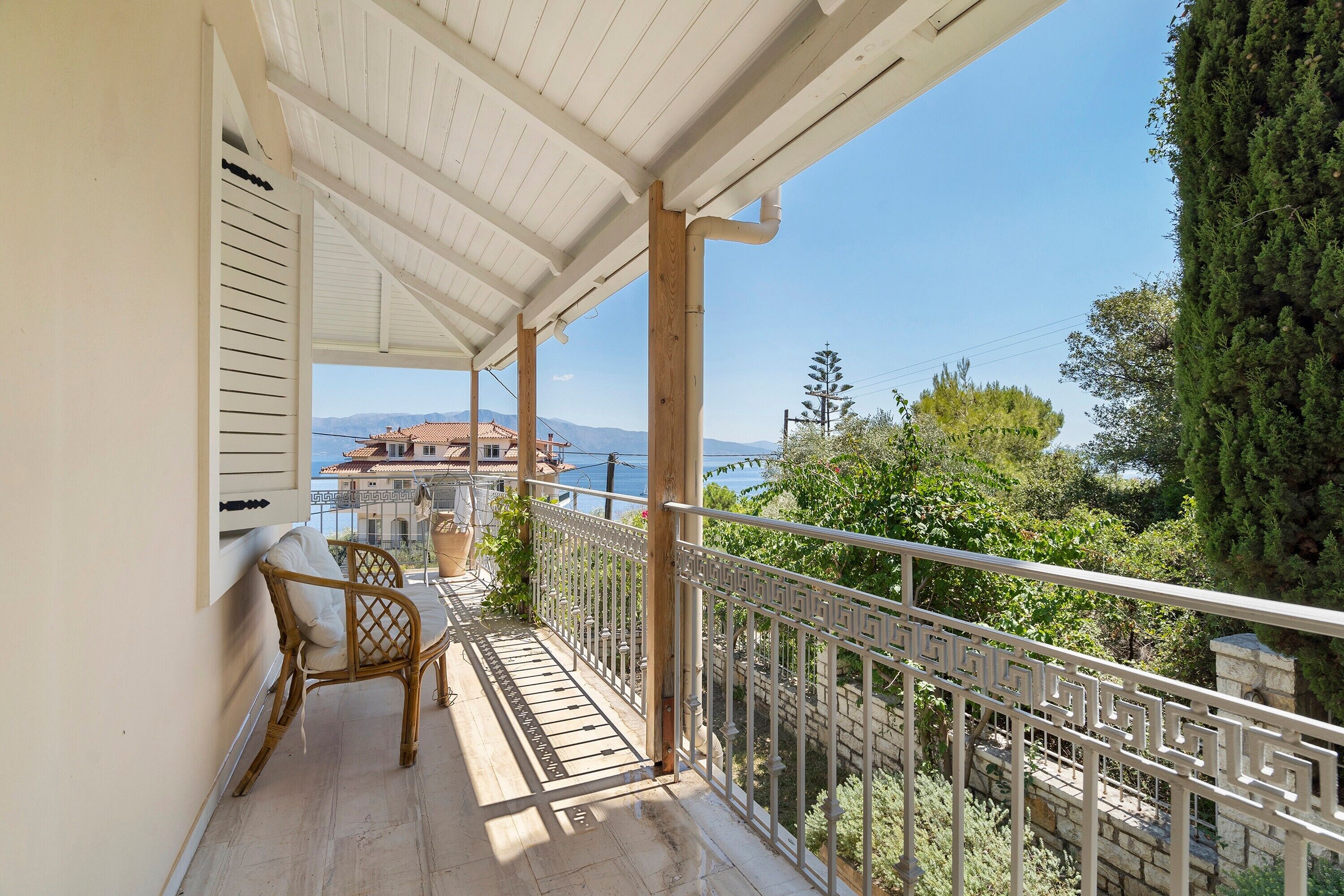 A balcony with a view of a coastal town, a wicker chair, and a railing.