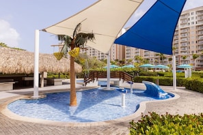 A swimming pool with a wave feature, palm trees, and a thatched roof structure.
