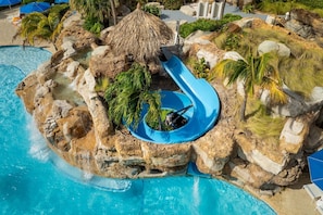 Une piscine avec un toboggan bleu, entourée de rochers et de palmiers.