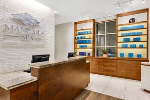 A reception area with a wooden reception desk, a white wall with a 'MANDARA SPA' sign, and shelves with blue boxes. - Marriott's Aruba Surf Club is on the oceanfront. T (Noord)
