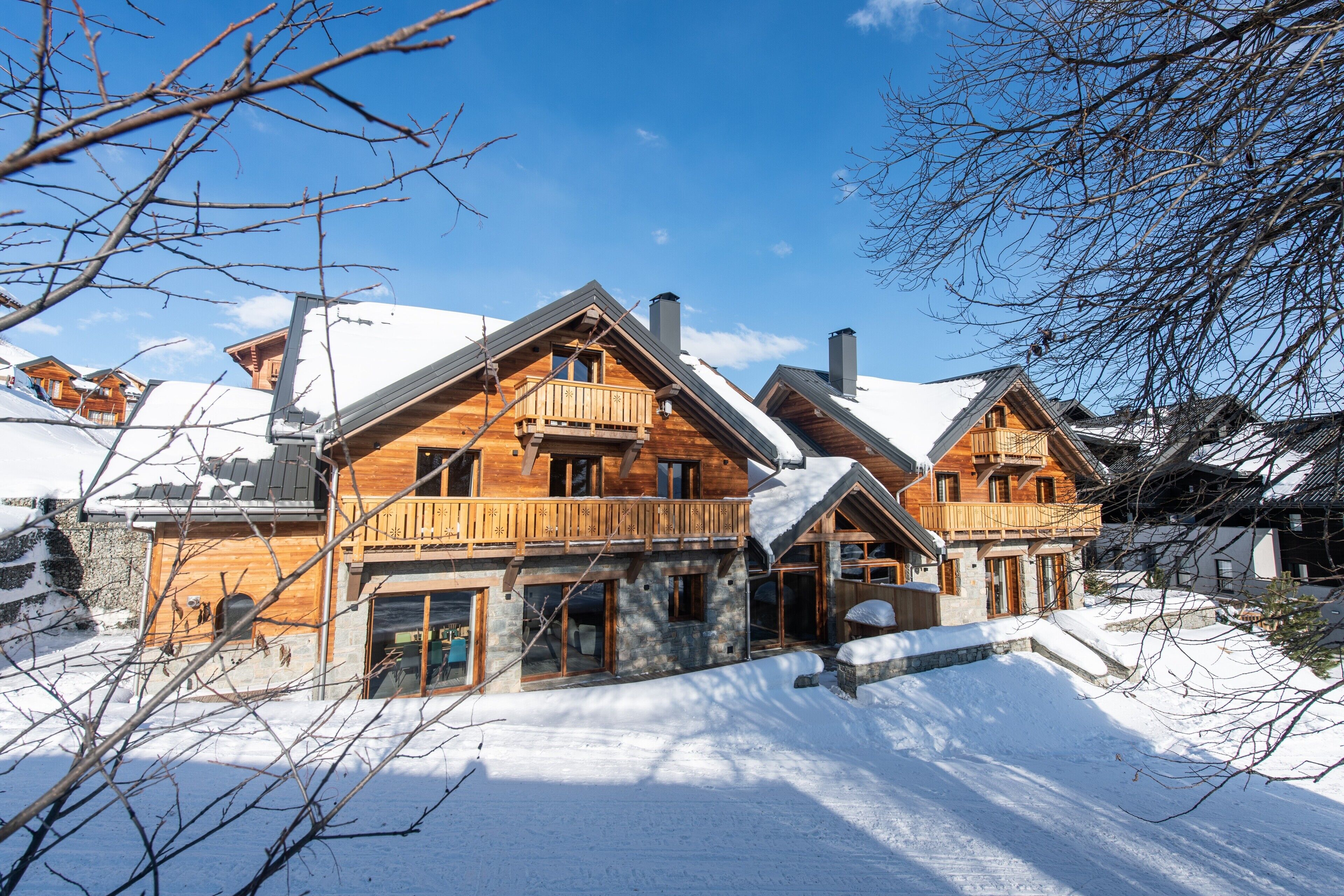 Un chalet en bois doté d’un balcon, de fondations en pierre et d’un toit recouvert de neige.