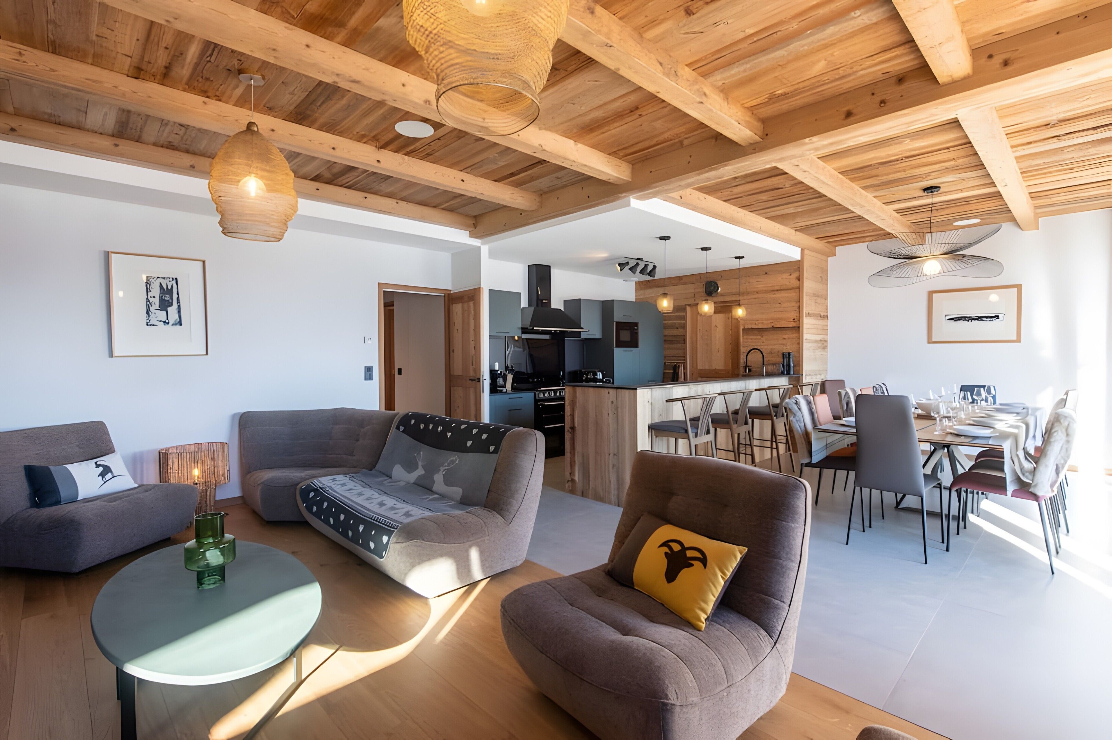 Una sala de estar moderna con un sofá, un sillón y una mesa redonda. Se ve una cocina y comedor al fondo.