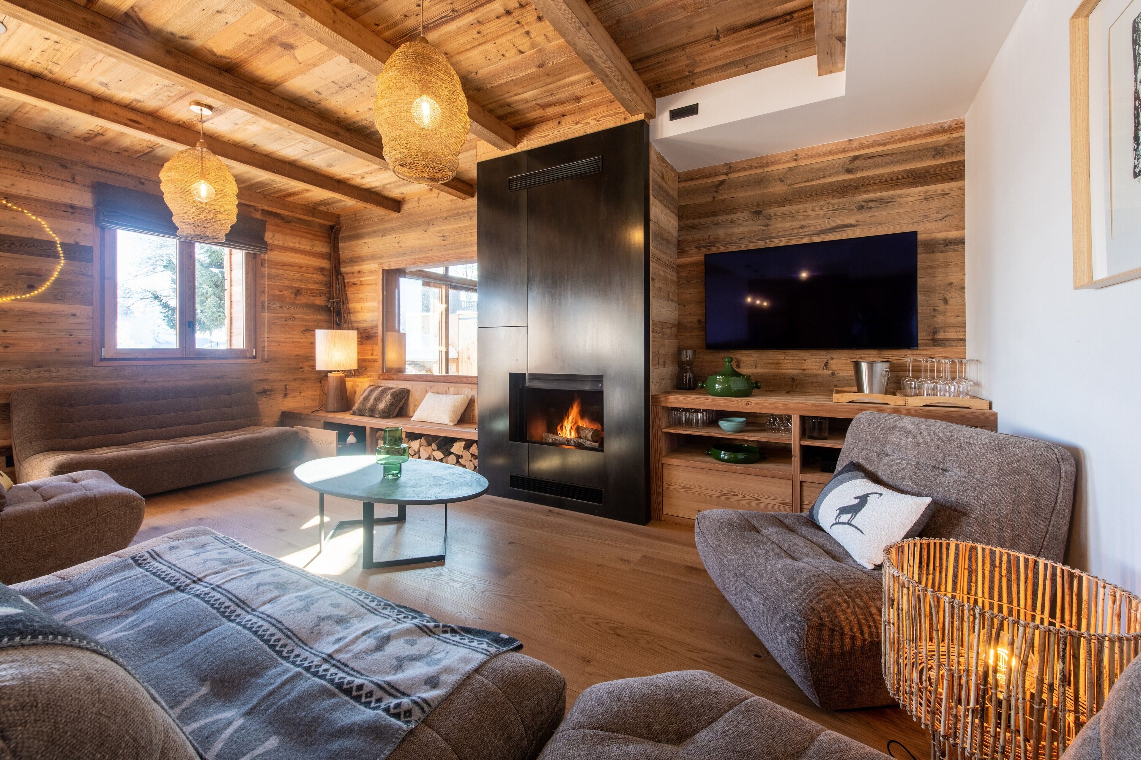 A modern living room with wooden beams, a fireplace, a flat-screen TV, and comfortable seating.