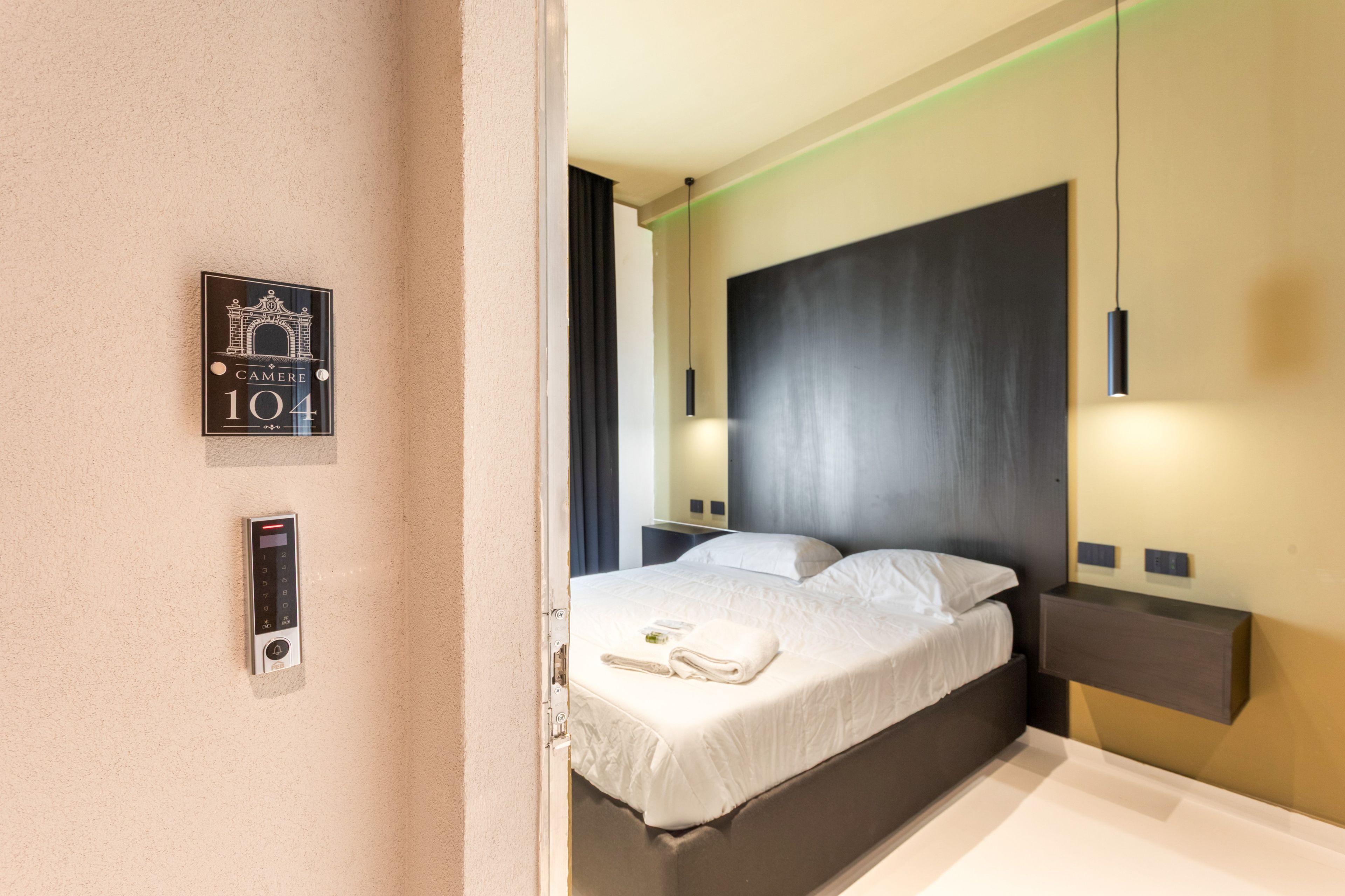 Una camera d'albergo con un letto, un telefono fissato al muro e una targa con il numero 101.