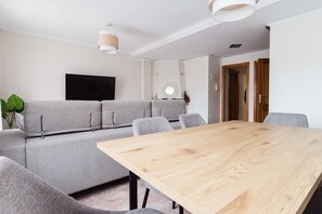 Una sala moderna con un sofá modular, una mesa de comedor de madera y un televisor de pantalla plana montado en la pared.