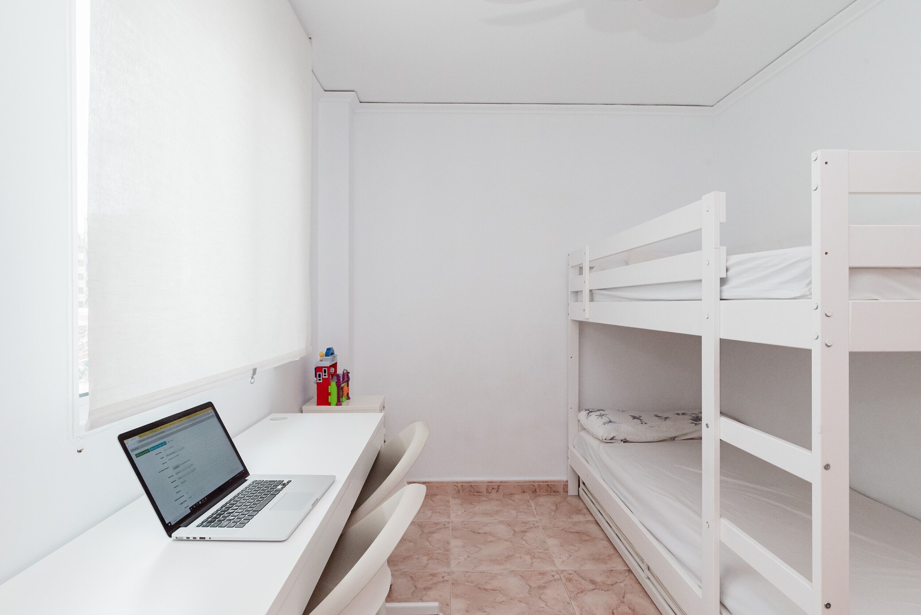 A room with a white desk, a laptop, bunk beds, and a small toy house on the wall.