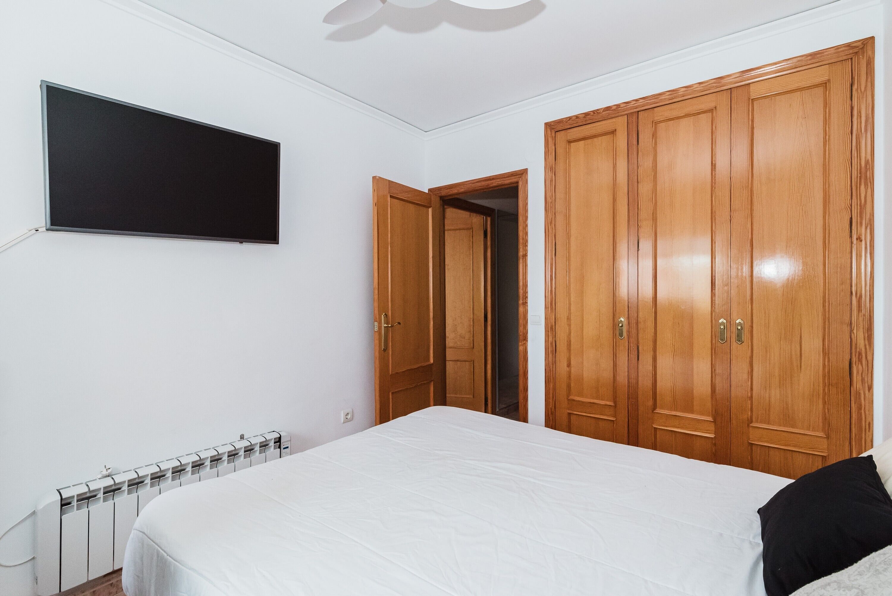 A bedroom with a bed, a wardrobe, a television, and a radiator.