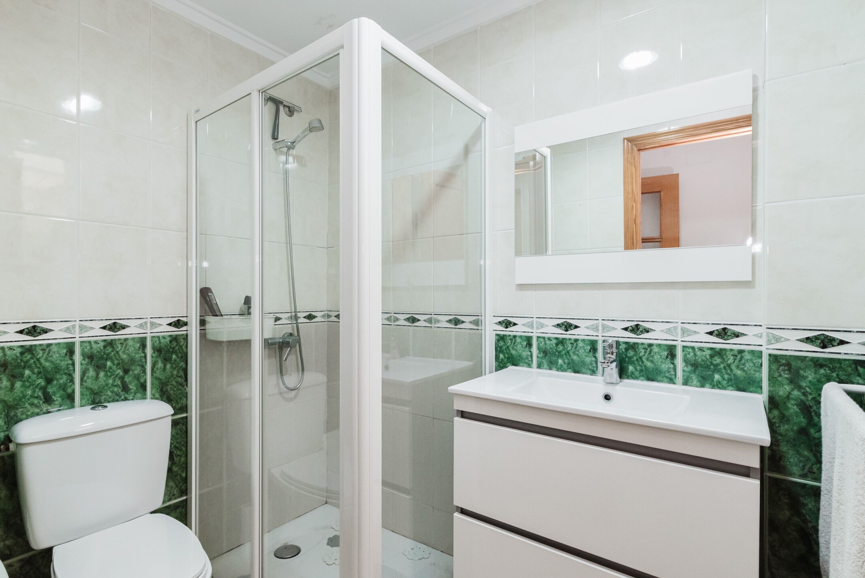 Un baño con ducha de vidrio, un lavamanos blanco y un espejo encima.