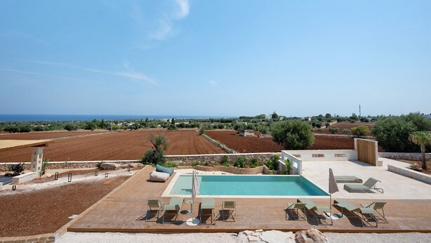 A pool area with lounge chairs and a view of the sea.