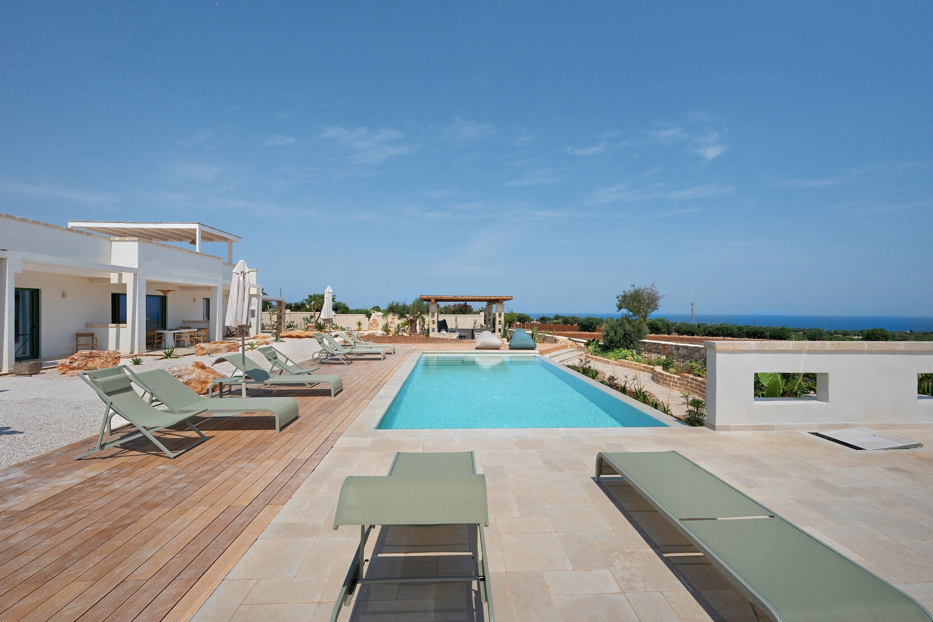 A pool area with lounge chairs and a view of the sea.