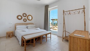 A bedroom with a bed, a bedside table, a bench, a drying rack, and a view of the outdoors.