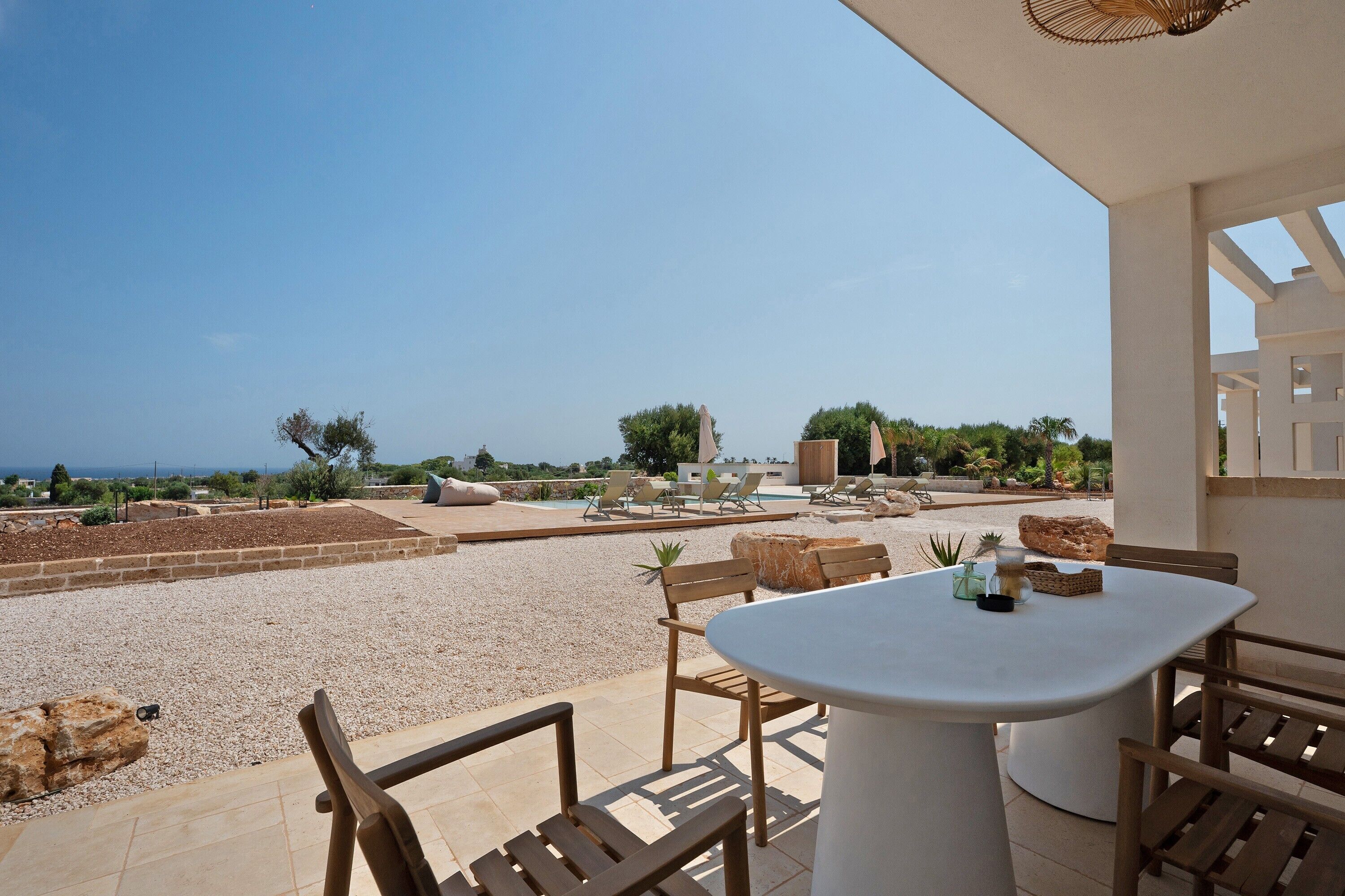 Une terrasse avec une table et des chaises, un espace piscine avec des chaises longues et une vue sur la mer.