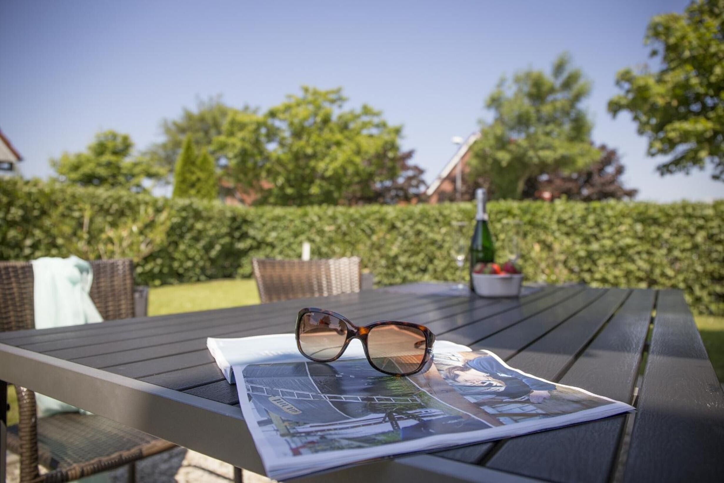 Un magazine et une paire de lunettes de soleil posées sur une table à l’extérieur.