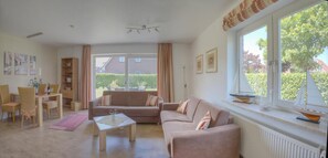 A living room with a sofa, a coffee table, and a dining area with chairs and a table. - Apartment Amrumbank Terrace with Private Garden, Terrace, and Wi-Fi (Büsum)
