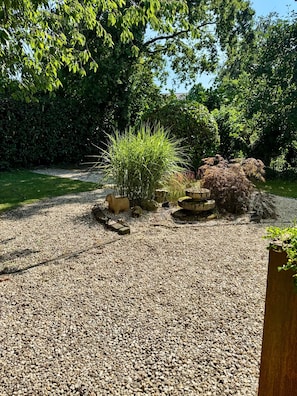Ein Kiesgarten mit einem kleinen Teich, umgeben von dichtem Grün und Bäumen.