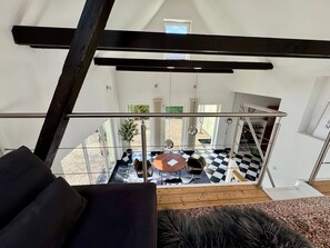 Un interior moderno con un sofá negro, suelo a cuadros, una escalera y vistas al exterior.