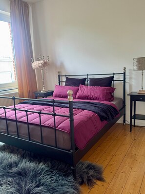 A bed with a black frame, a fluffy rug, and a window with curtains. - Holiday Home 'Haus um 1900 – Entire Place for You' with Terrace, Garden & Wi-Fi (Ennigerloh)