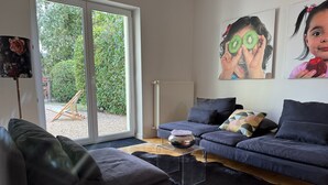 Uma sala de estar moderna com um sofá cinza, uma poltrona de couro preto e um tapete felpudo preto. Há uma mesa de centro de vidro transparente com uma tigela decorativa sobre ela.