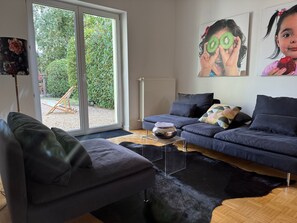 Ein modernes Wohnzimmer mit einem grauen Sofa, einem schwarzen Ledersessel und einem schwarzen, flauschigen Teppich. Ein klarer Glastisch mit einer dekorativen Schale darauf.