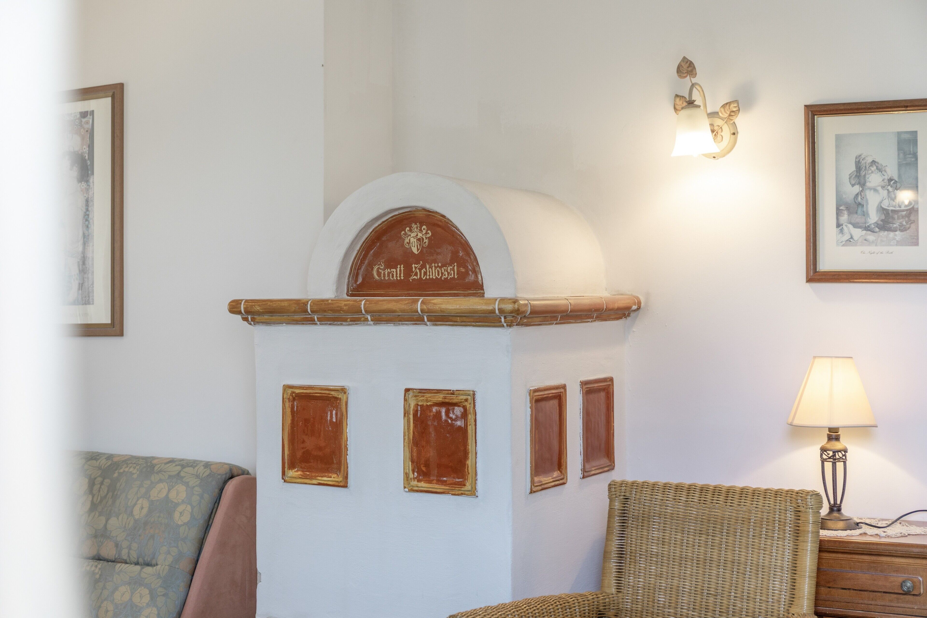Een kamer met een open haard, ingelijste foto's, een lamp en een rieten stoel.