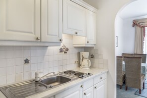 A kitchen with white cabinets, a coffee maker, a sink, and a dining area with wicker chairs. - Apartment "Grattschlössl 1" with Mountain View, Balcony, and Wi-Fi (Sankt Johann)