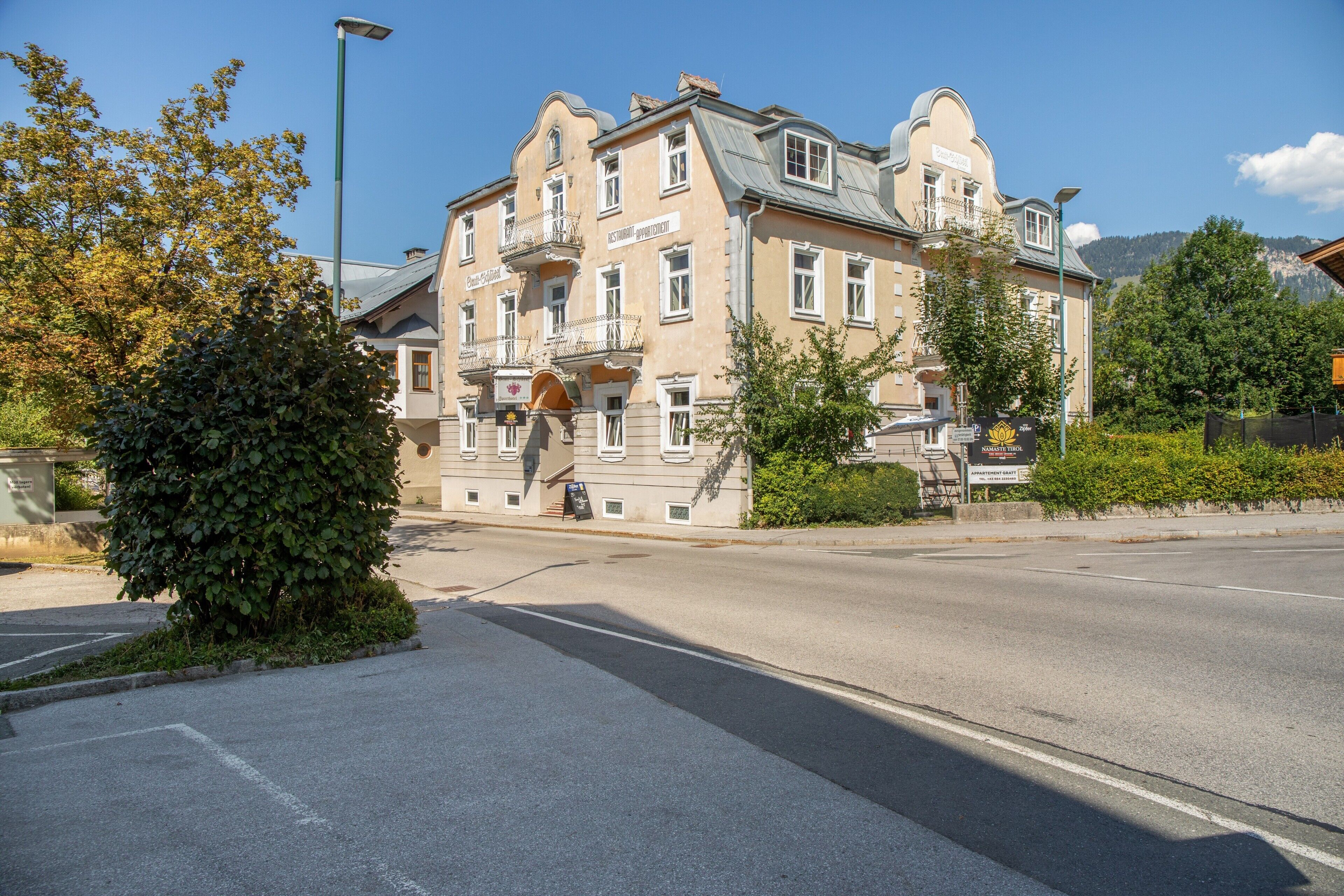 En bygning med flere etager, med et skilt der viser restaurant og lejligheder, en gade foran og træer.