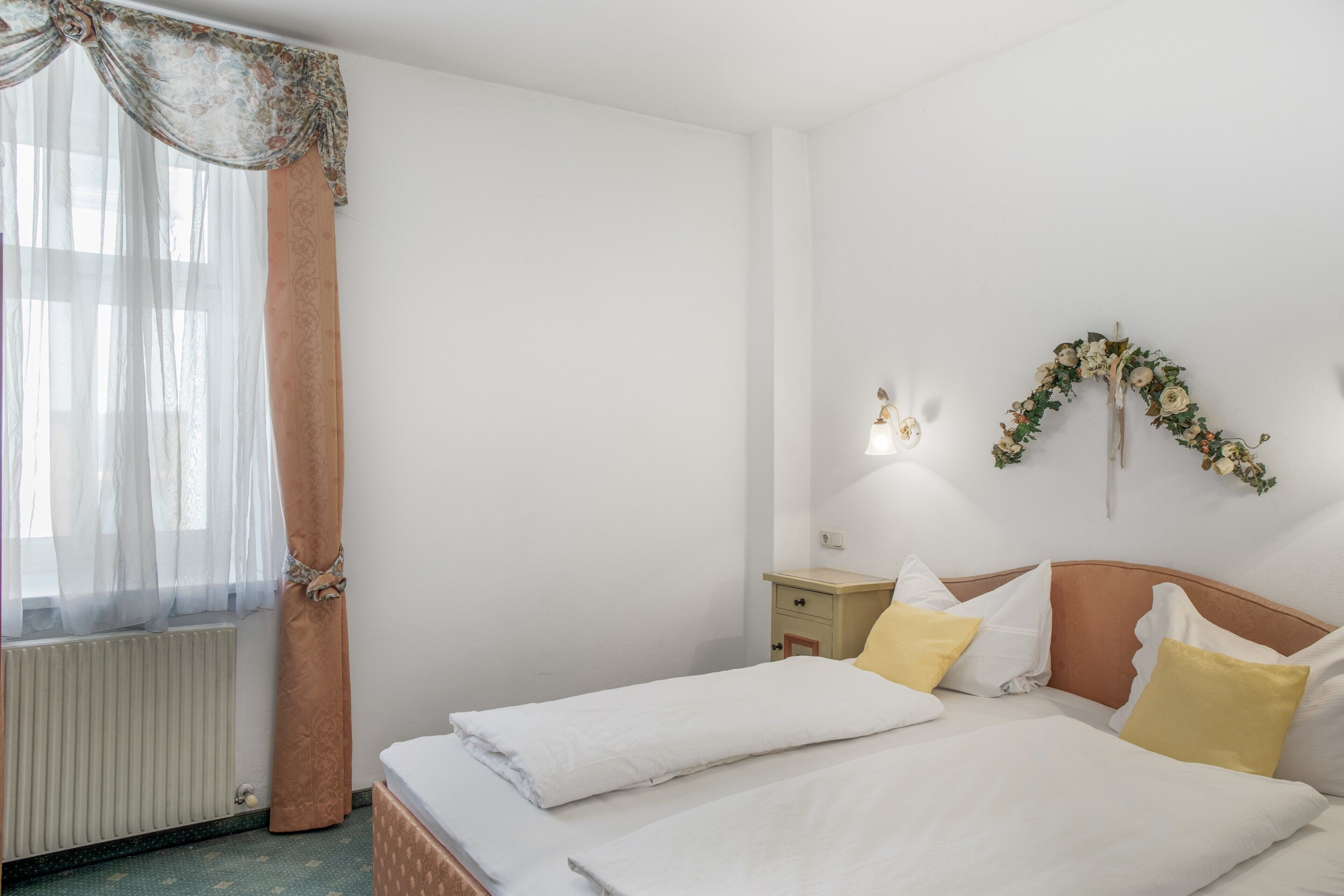 Hotelkamer met een bed, nachtkastje, wandlamp en een decoratieve bloemenstelling.