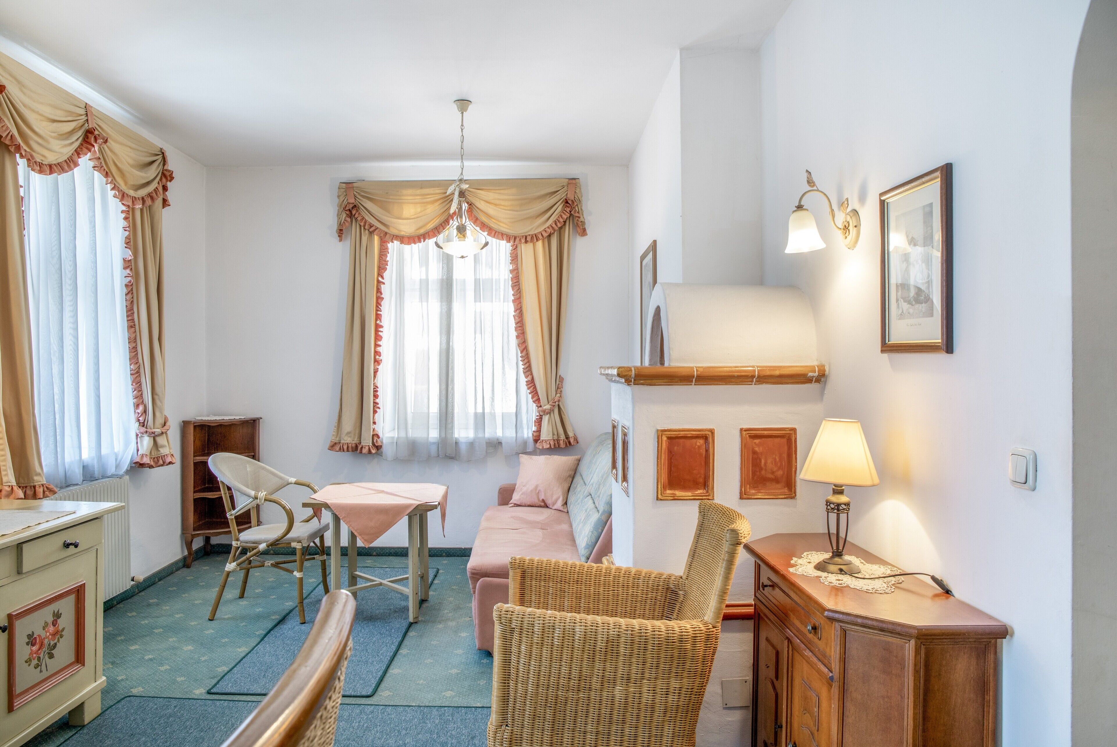 Une pièce comprenant une table à manger, deux chaises, un canapé, un fauteuil en osier, un meuble et une lampe fixée au mur.