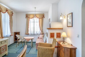 A room with a dining table, two chairs, a sofa, a wicker chair, a cabinet, and a wall-mounted lamp. - Apartment "Grattschlössl 1" with Mountain View, Balcony, and Wi-Fi (Sankt Johann)