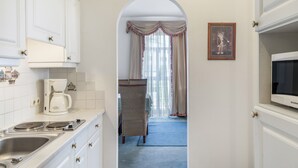A narrow hallway with a kitchen area on one side, a wicker chair, and a framed picture on the wall. - Apartment “Grattschlössl 1” with Mountain View, Balcony, and Wi-Fi (Sankt Johann)