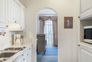 A narrow hallway with a kitchen area on one side, a wicker chair, and a framed picture on the wall. - Apartment “Grattschlössl 1” with Mountain View, Balcony, and Wi-Fi (Sankt Johann)