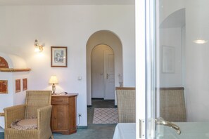A room with a wicker chair, a small wooden cabinet, a framed picture on the wall, and a doorway leading to another room. - Apartment "Grattschlössl 1" with Mountain View, Balcony, and Wi-Fi (Sankt Johann)