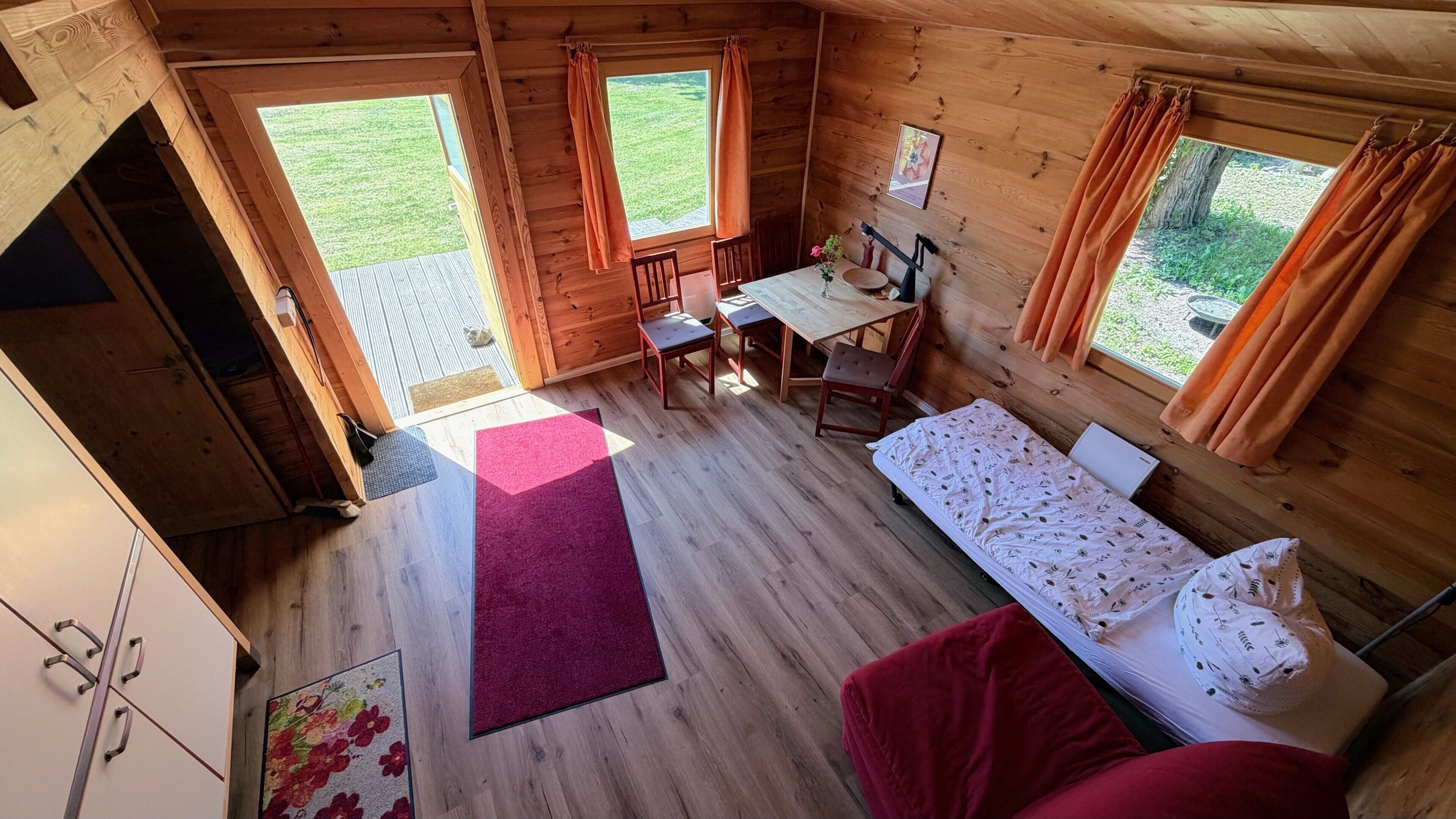 A cabin with a wooden interior, a bed, a desk with a chair, and a view of the outdoors.