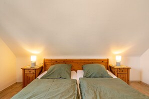 Habitación doble con dos camas, cabeceros de madera, mesitas de noche con lámparas y suelo de madera.