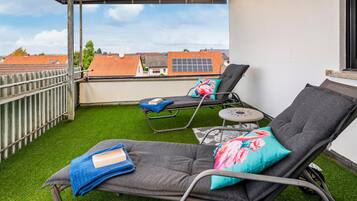A balcony with two lounge chairs, one with a blue towel and a book, and the other with a pink floral pillow.