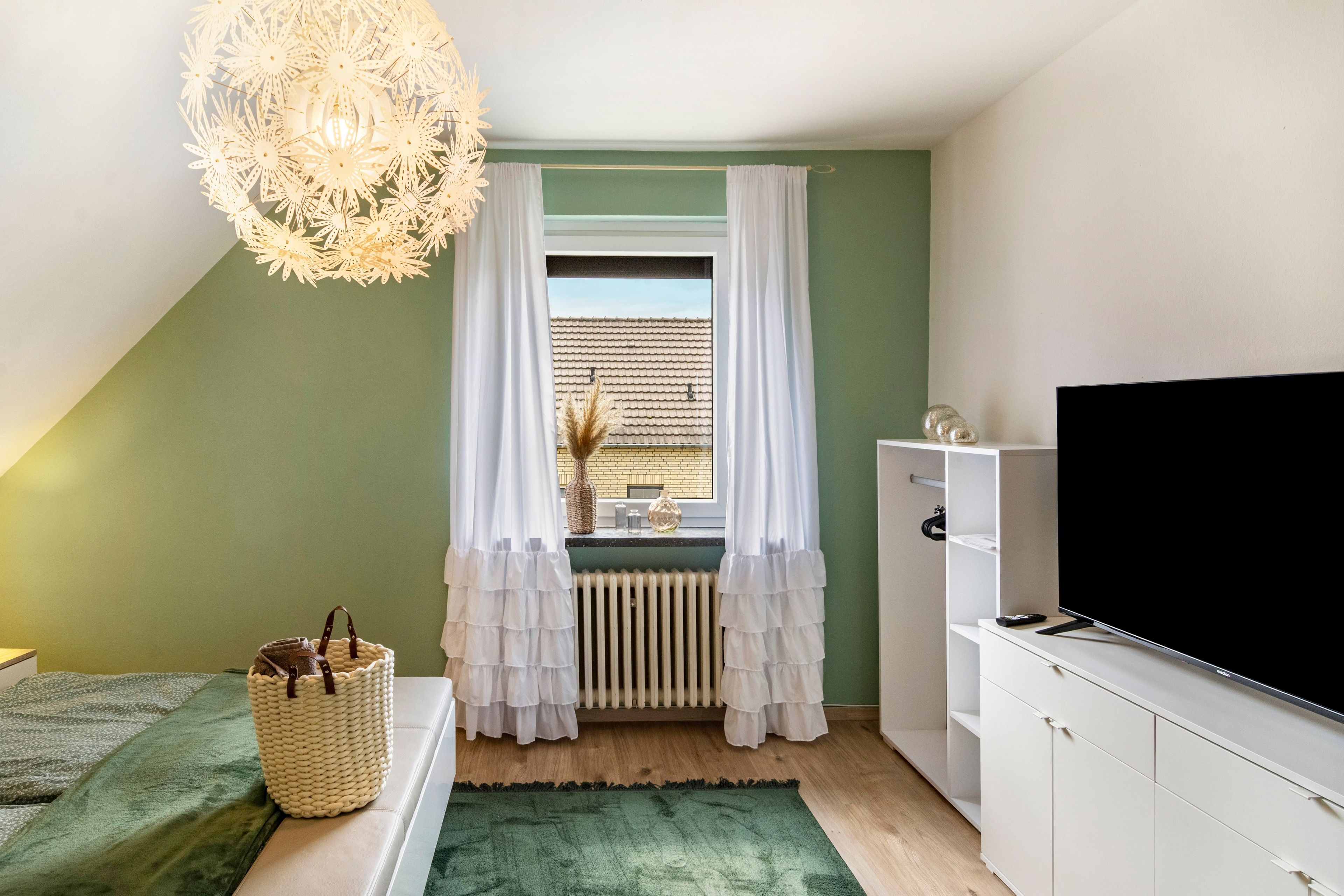 Ein Schlafzimmer mit einem Bett, einem Fernseher, einem Heizkörper und einem Fenster mit Vorhängen.