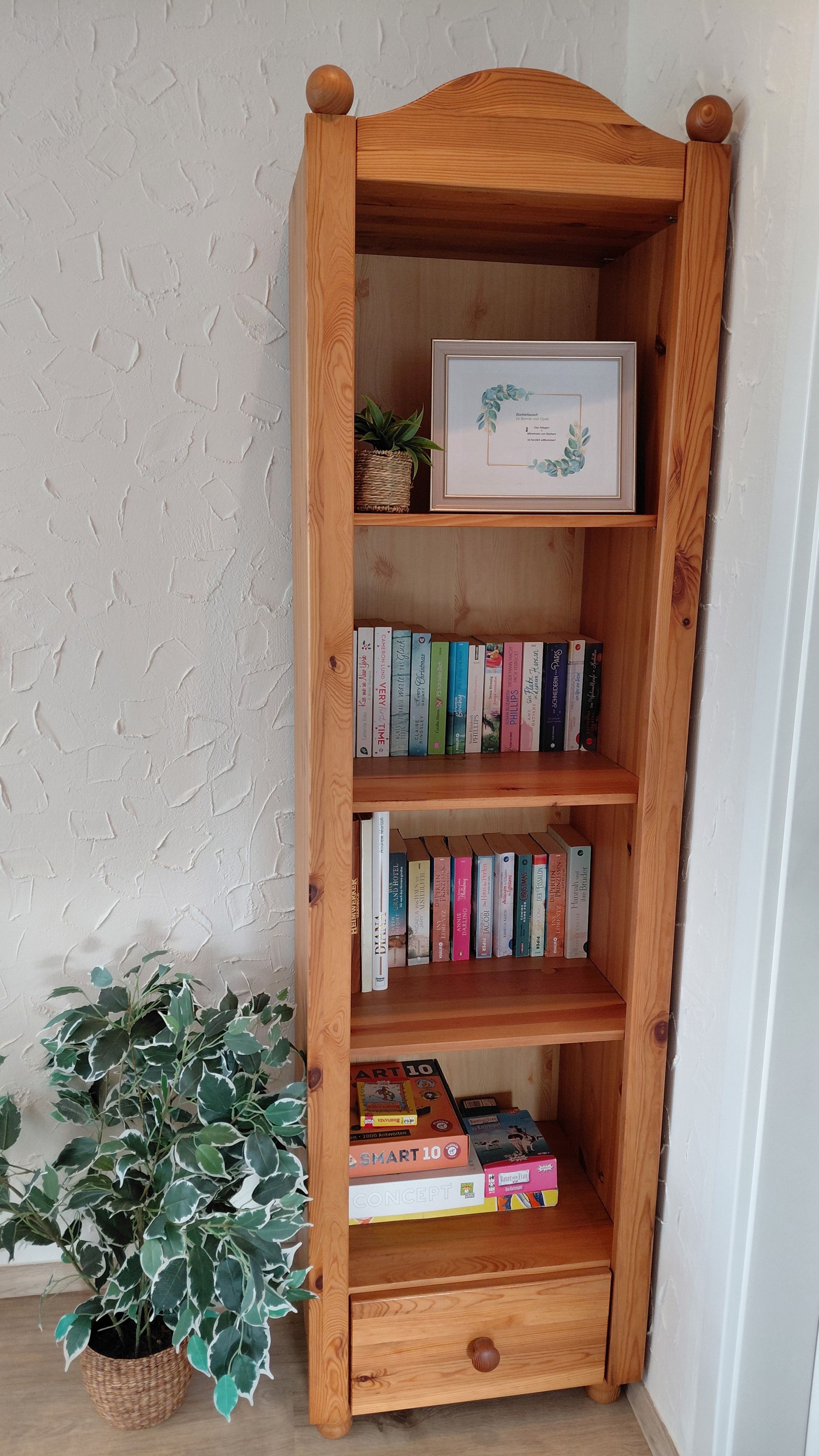 Une bibliothèque en bois avec plusieurs étagères, un certificat encadré et une plante en pot.