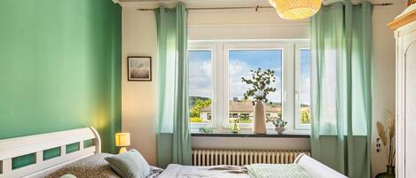 A bedroom with a bed, a window with curtains, a radiator, and a hanging light fixture.