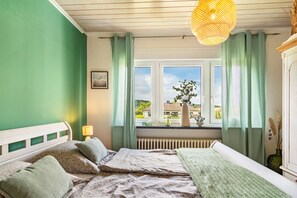 Une chambre à coucher avec un lit, une fenêtre avec des rideaux, un radiateur et un luminaire suspendu.