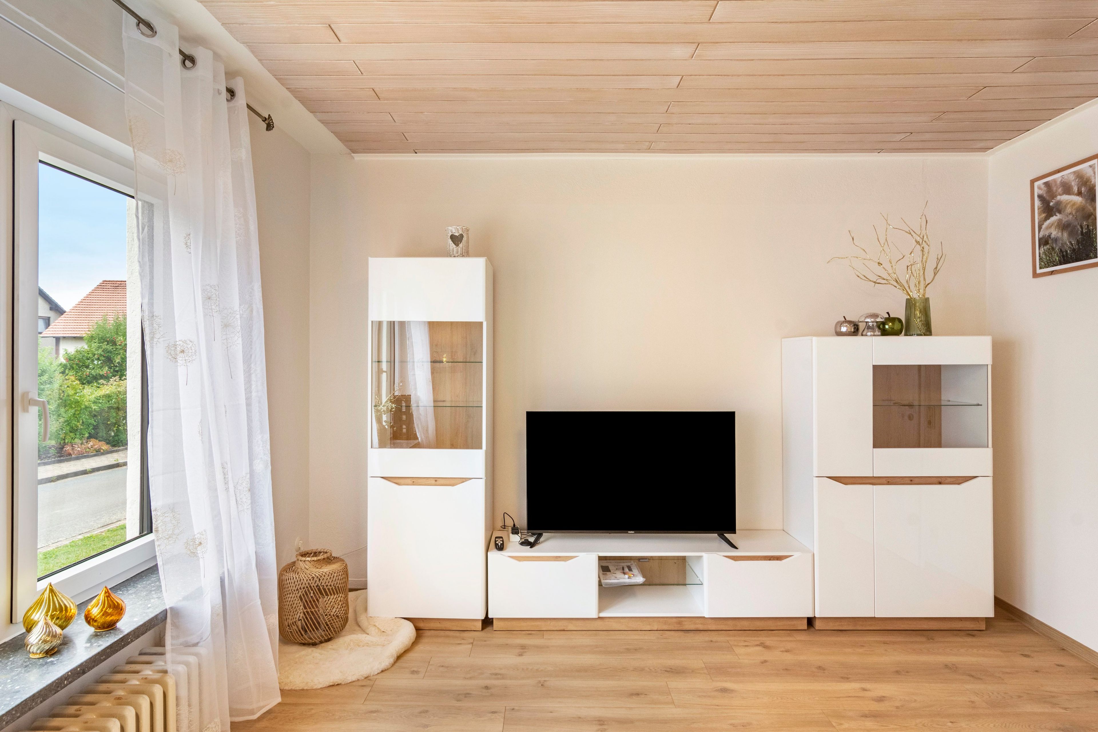 A modern living room with a flat-screen TV, built-in shelving, and a large window with curtains.