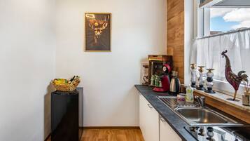Une cuisine avec un plancher en bois, un réfrigérateur noir, un évier et une fenêtre donnant sur le ciel.