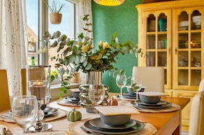 Een eettafel gedekt met borden, kommen en glazen, een vaas met bloemen en een kaars.