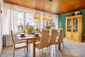A dining area with a wooden table set for four, surrounded by chairs, with a green wall and a wooden cabinet in the background. - Holiday Home 'By Bonnie und Clyde' with Mountain View, Private Terrace and Wi-Fi (Duderstadt)