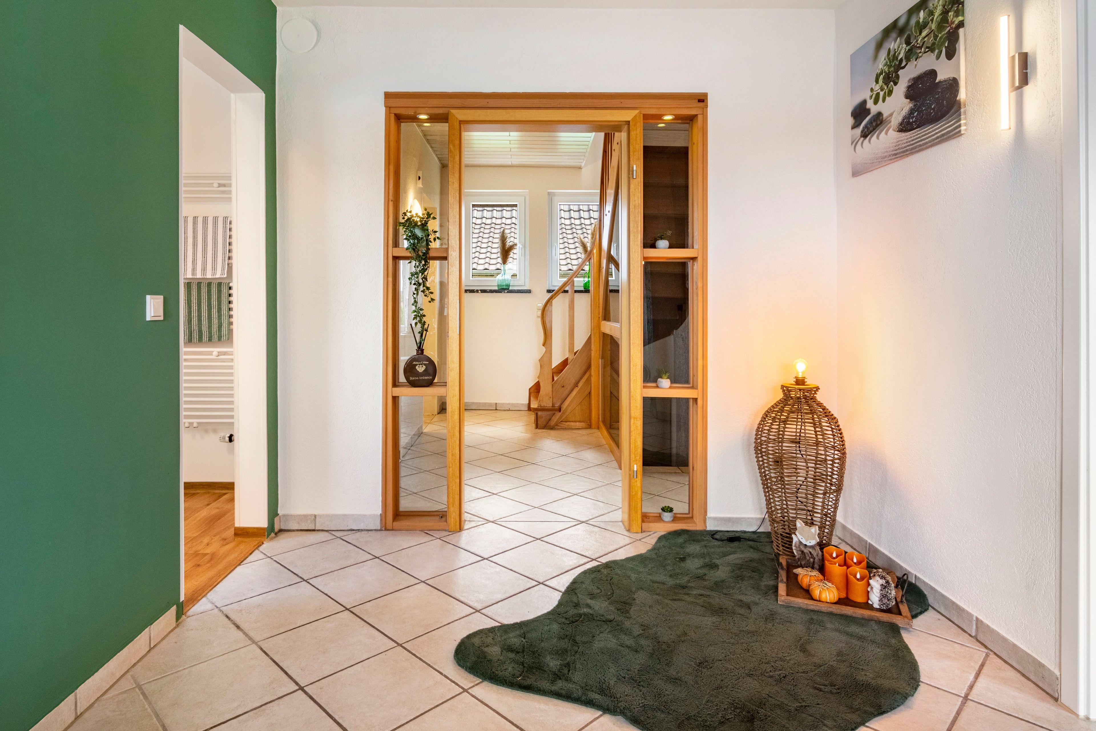 A hallway with a green wall, a wooden door, a tiled floor, and a small rug.