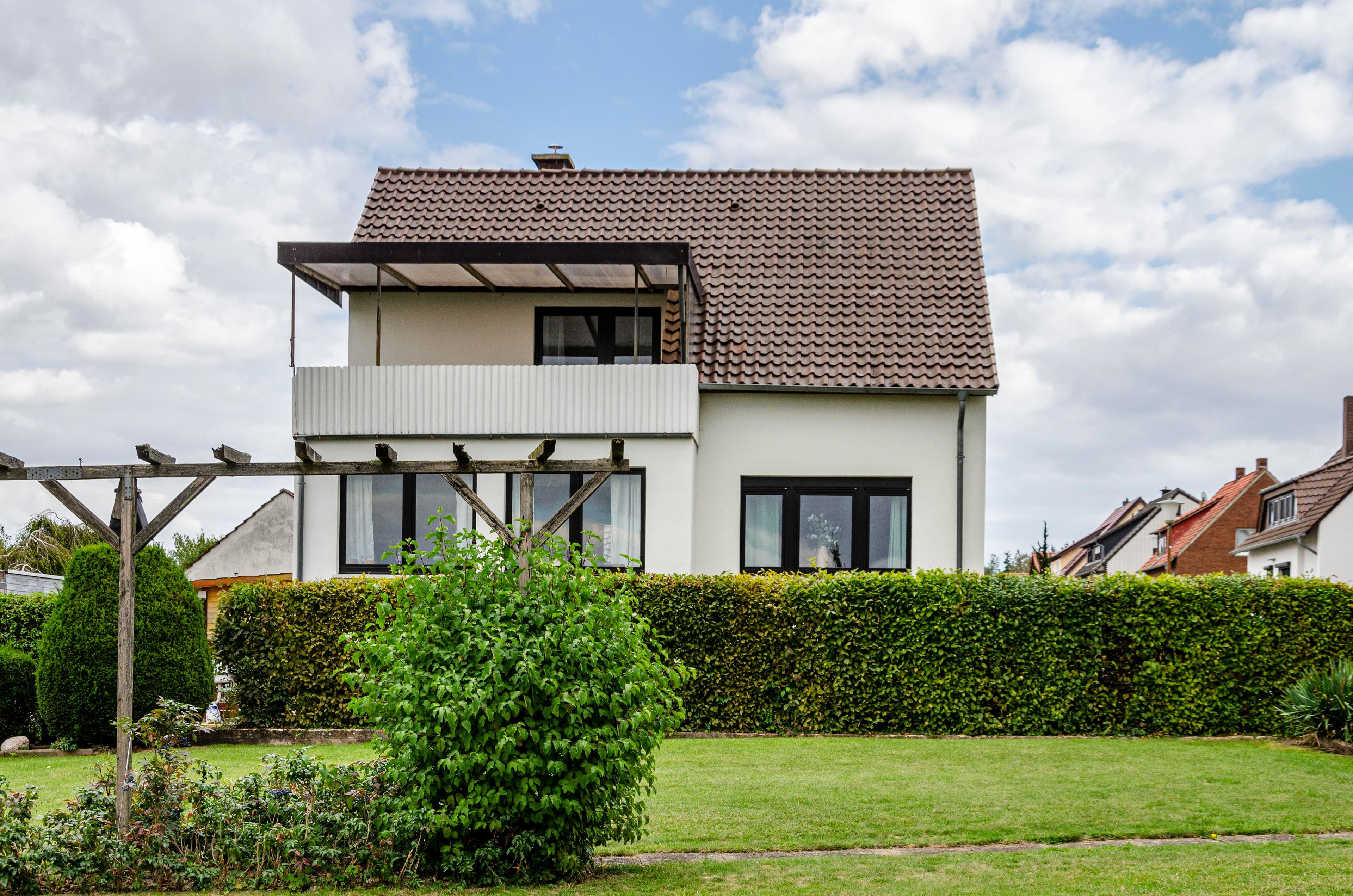 Une maison à deux étages, avec un toit en tuiles, un balcon bien visible et un jardin bien entretenu.