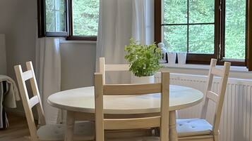 Een eetgedeelte met een ronde tafel, vier houten stoelen, een hanglamp en een raam met uitzicht op groen.