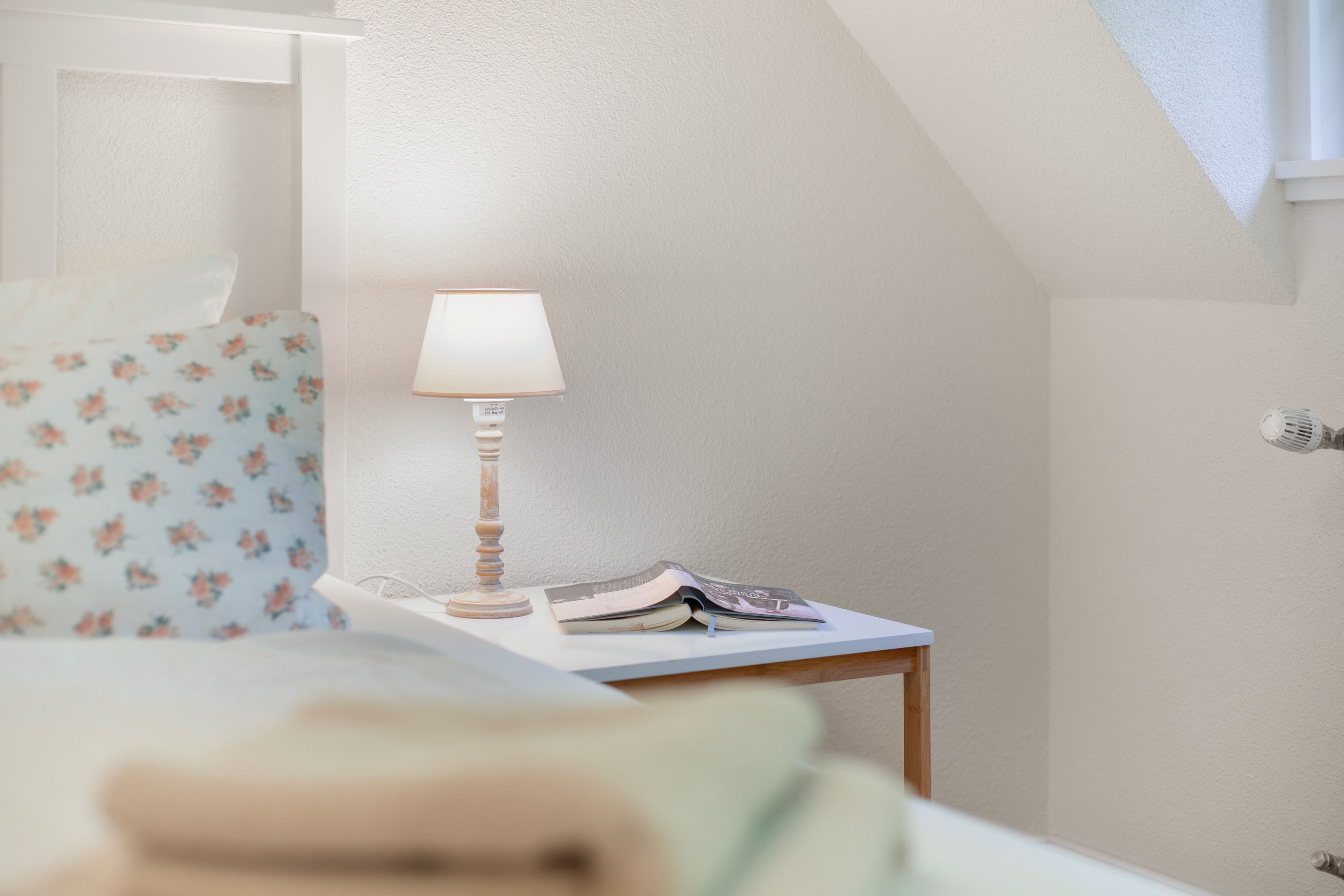 Un dormitorio con una cama, una mesita de noche con lámpara y una silla de estampado floral.